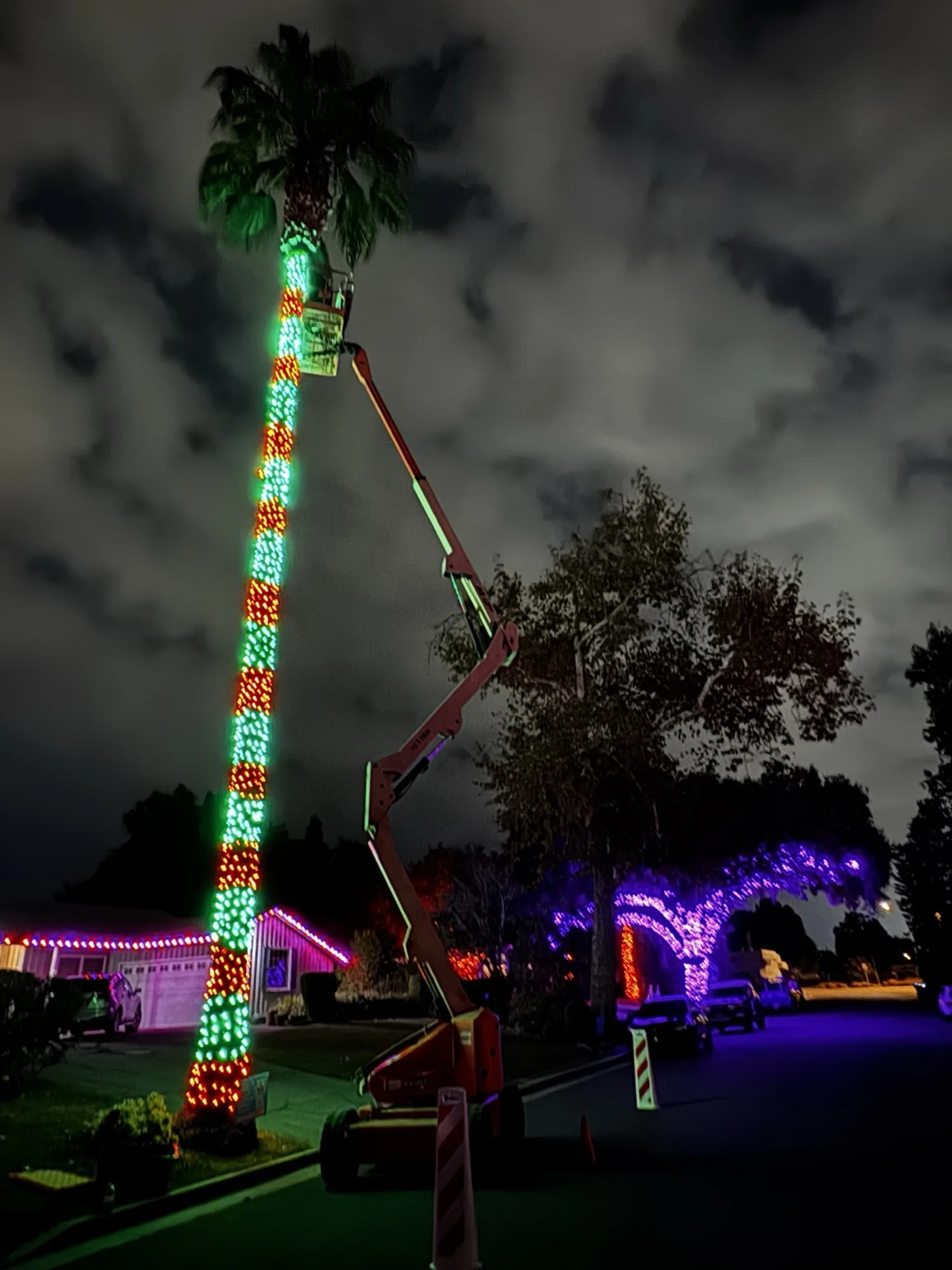 Bee Merry technician on a boom lift installing Christmas lights safely at night instead of a homeowner on a ladder