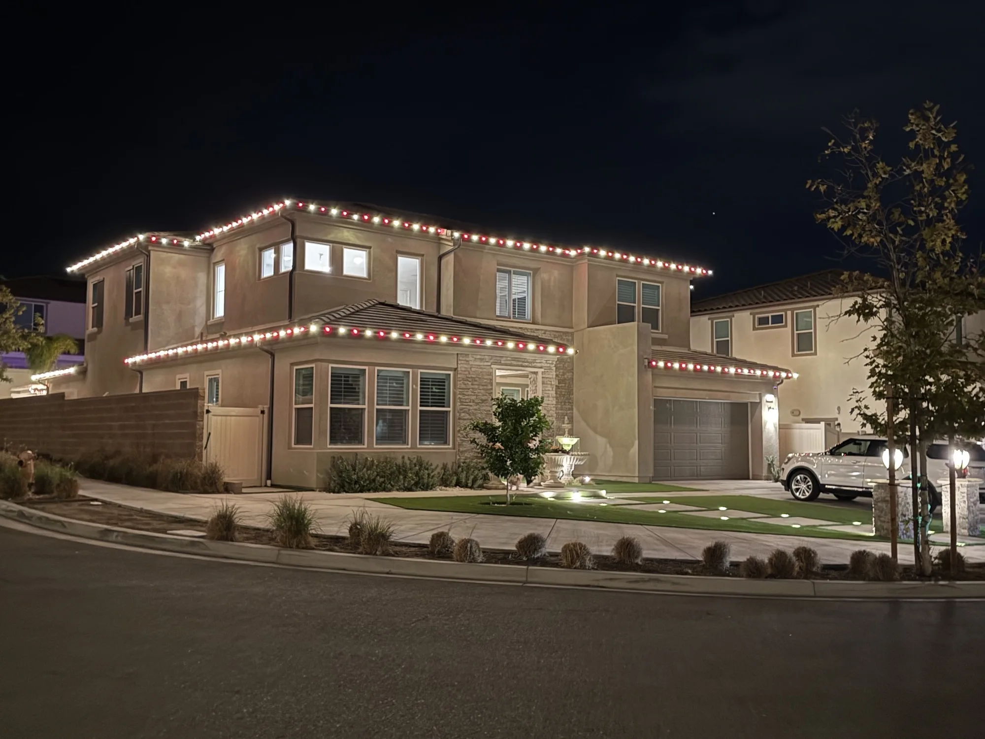 Venue exterior with warm accent lighting and a lit fountain by Bee Merry